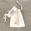 An Amy Wing Designs jewelry gift bag laying on a concrete background, with a small business card with a photo of a hand stamped cuff sitting on top.